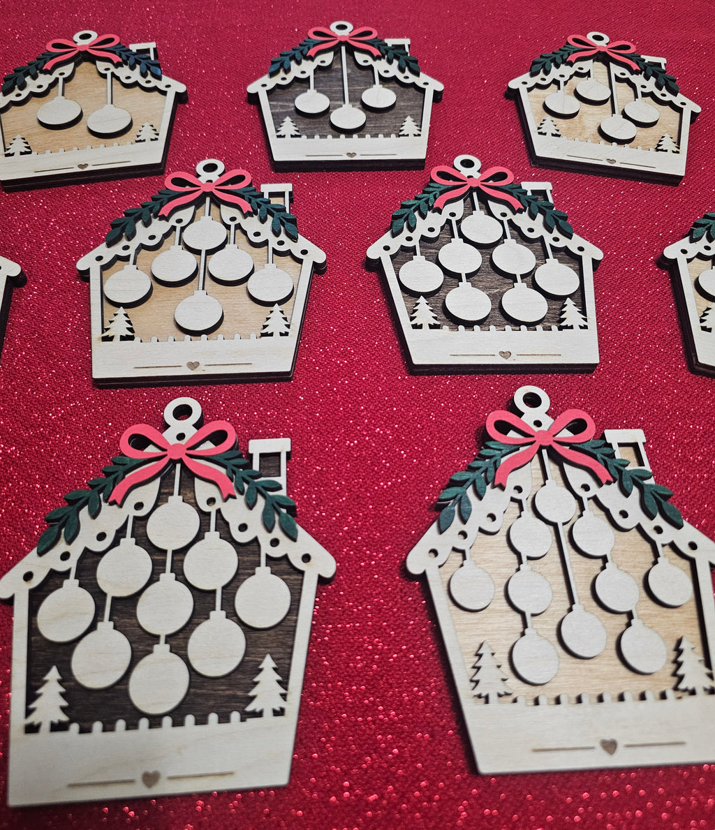 A set of laser-cut wooden Christmas ornament decorations shaped like houses, featuring green holly leaves, red bows, and hanging circular ornaments, arranged on a red glittery background.