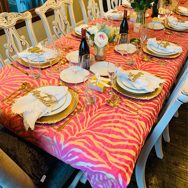 A pink and white zebra-print tablecloth draped over a long dining table, styled with gold charger plates, white plates, gold cutlery, wine glasses, and floral centerpieces.